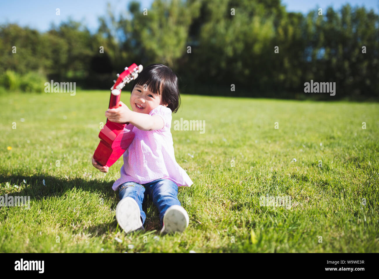 toddler girl playing guitar at sunny countryside home garden Stock