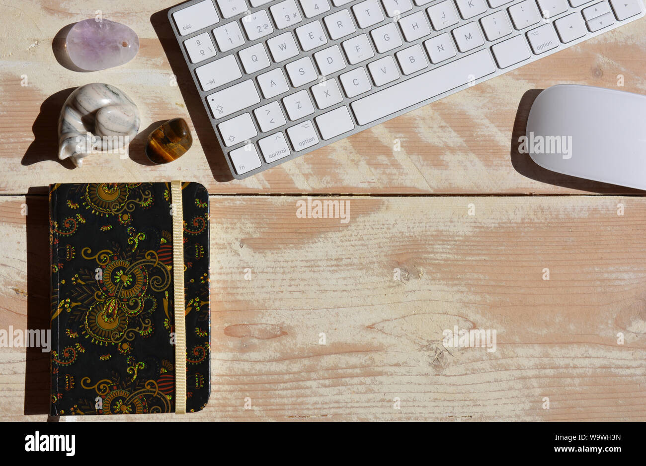 Modern workspace, wireless keyboard and mouse, notebook and semi precious gemstones including tiger's eye. Flat lay high angle view with copy space. Stock Photo