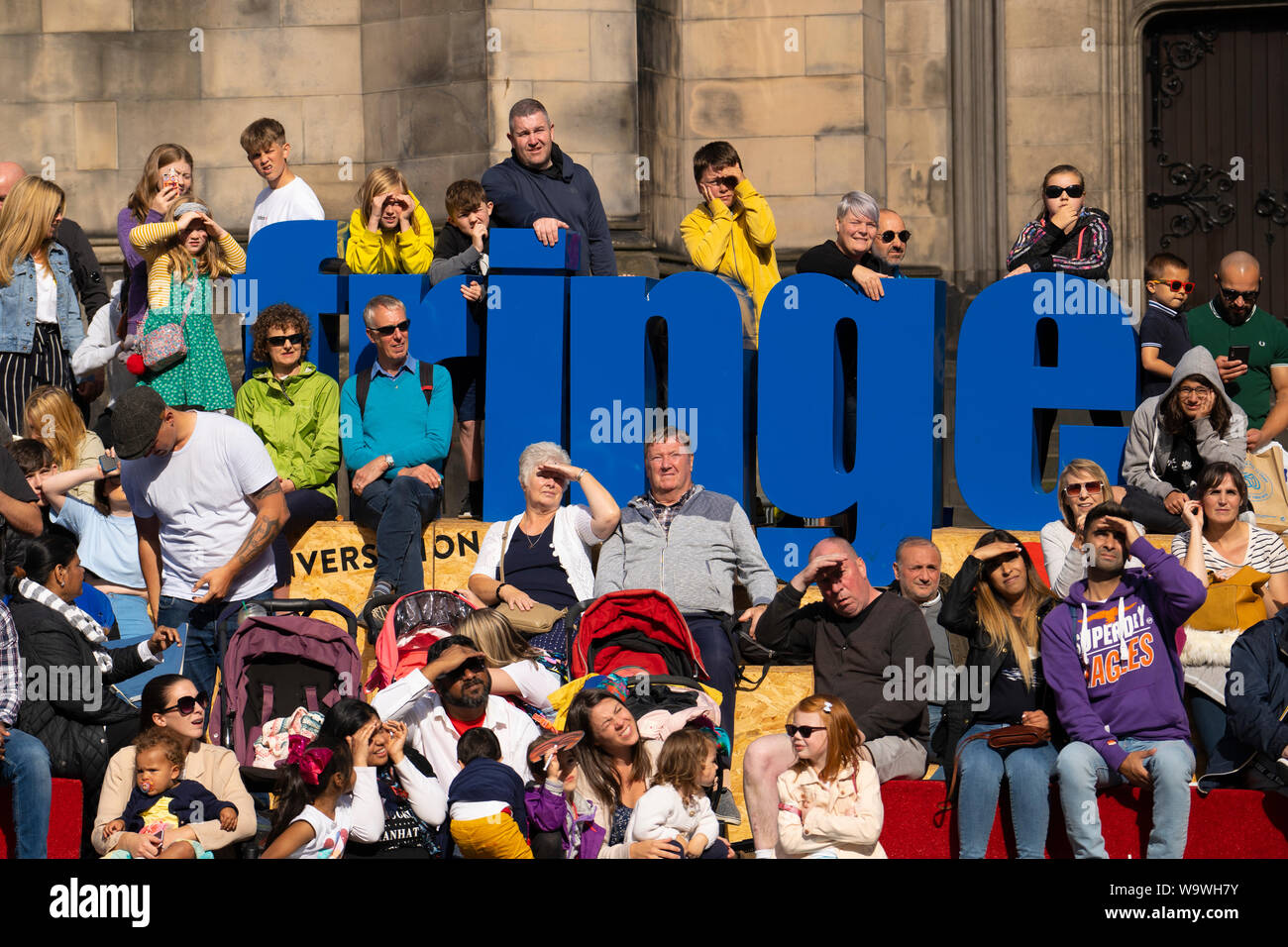 Edinburgh, Scotland, UK. 15 August 2019. Warm sunny weather in Edinburgh brought thousands of tourists onto the Royal Mile to enjoy the many street performers and actors promoting their shows during the Edinburgh Festival Fringe. Pictured. Audience watch a performer in West Parliament Square.  Iain Masterton/Alamy Live News Stock Photo