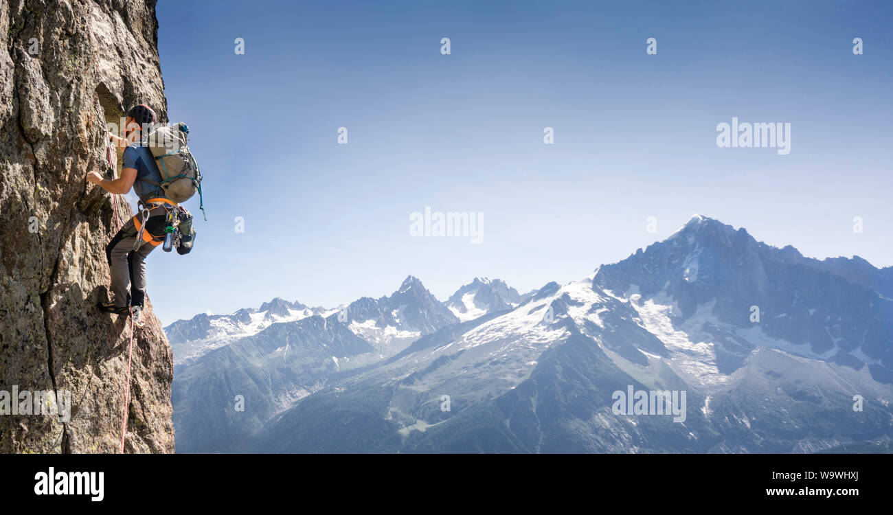 Young man rock climbing in Chamonix on the Clocher Clochetons Traverse on Brévent in front of a view of Mont Blanc. Aiguilles Rouges, French Alps. Stock Photo