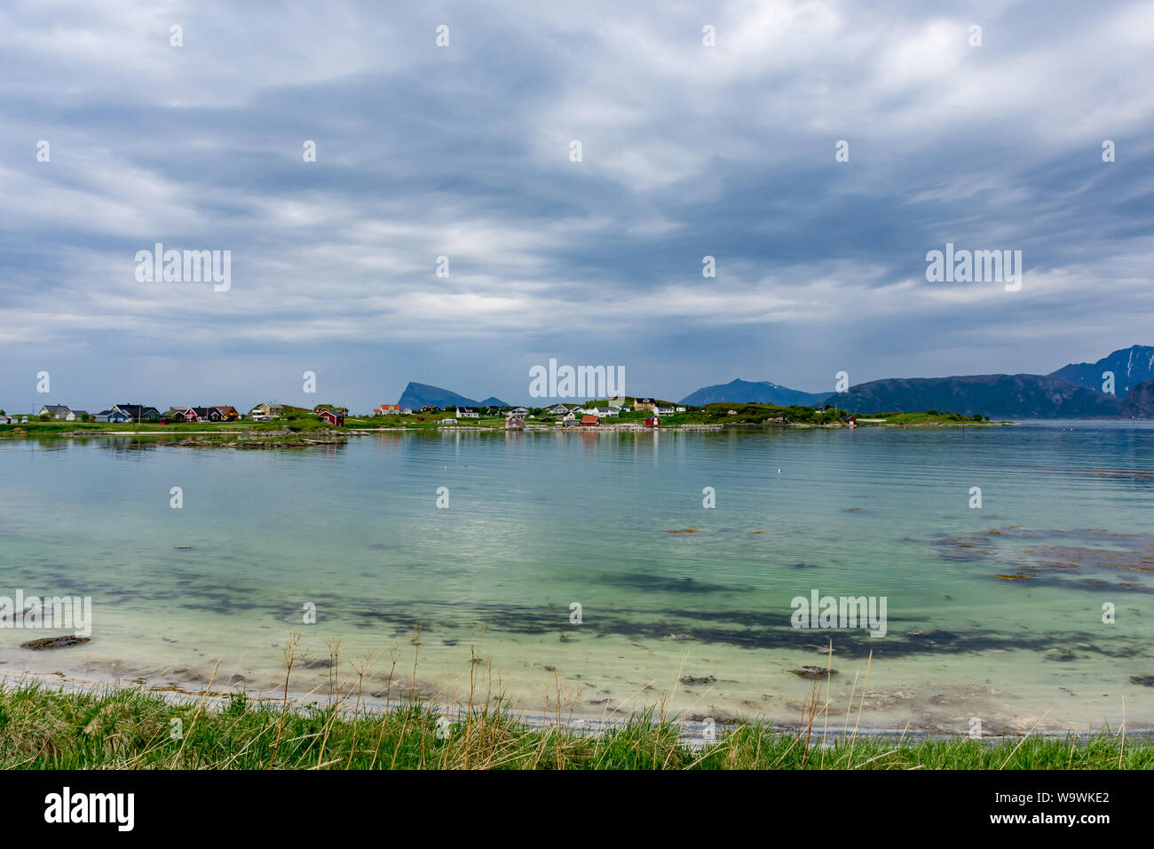 Bright coloured wooden houses across the clear waters of a sea loch near Sommaroy near Tromso in northern Norway Stock Photo
