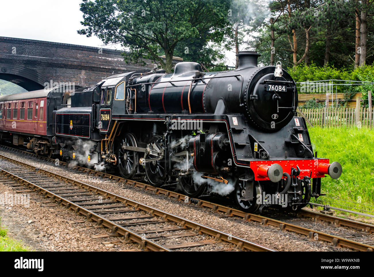 Locomotive no 76084 class 4MT as it rolls under the bridge at Weybourne station with a rake of carriages Stock Photo