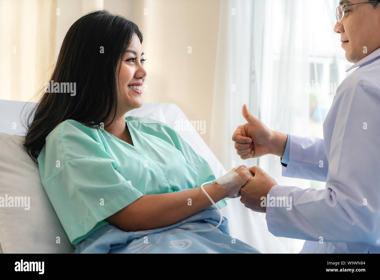 Hand of man doctor reassuring his female patient with thump up in bed at hospital. Medical ethics and trust concept. Stock Photo