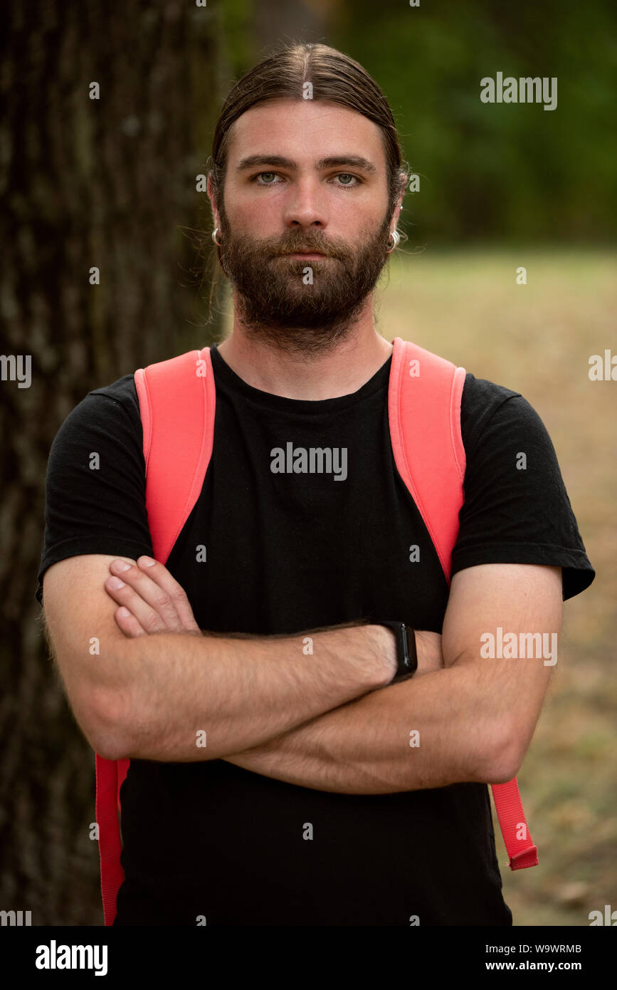 Portrait of young male in natural light looking defensive while holding his arms crossed and wearing a black shirt. Bearded caucasian man looking at t Stock Photo