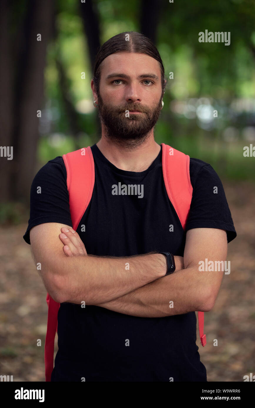 Portrait of young male in natural light looking defensive while holding his arms crossed and wearing a black shirt. Bearded caucasian man looking at t Stock Photo