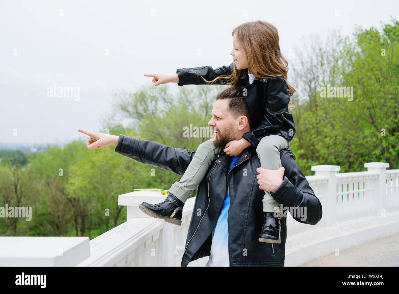 Fashionable stylish family for a walk. Dad rolls his daughter on his shoulders. Excursion. Indicate the direction.Travel and tourism concept. Time tog Stock Photo