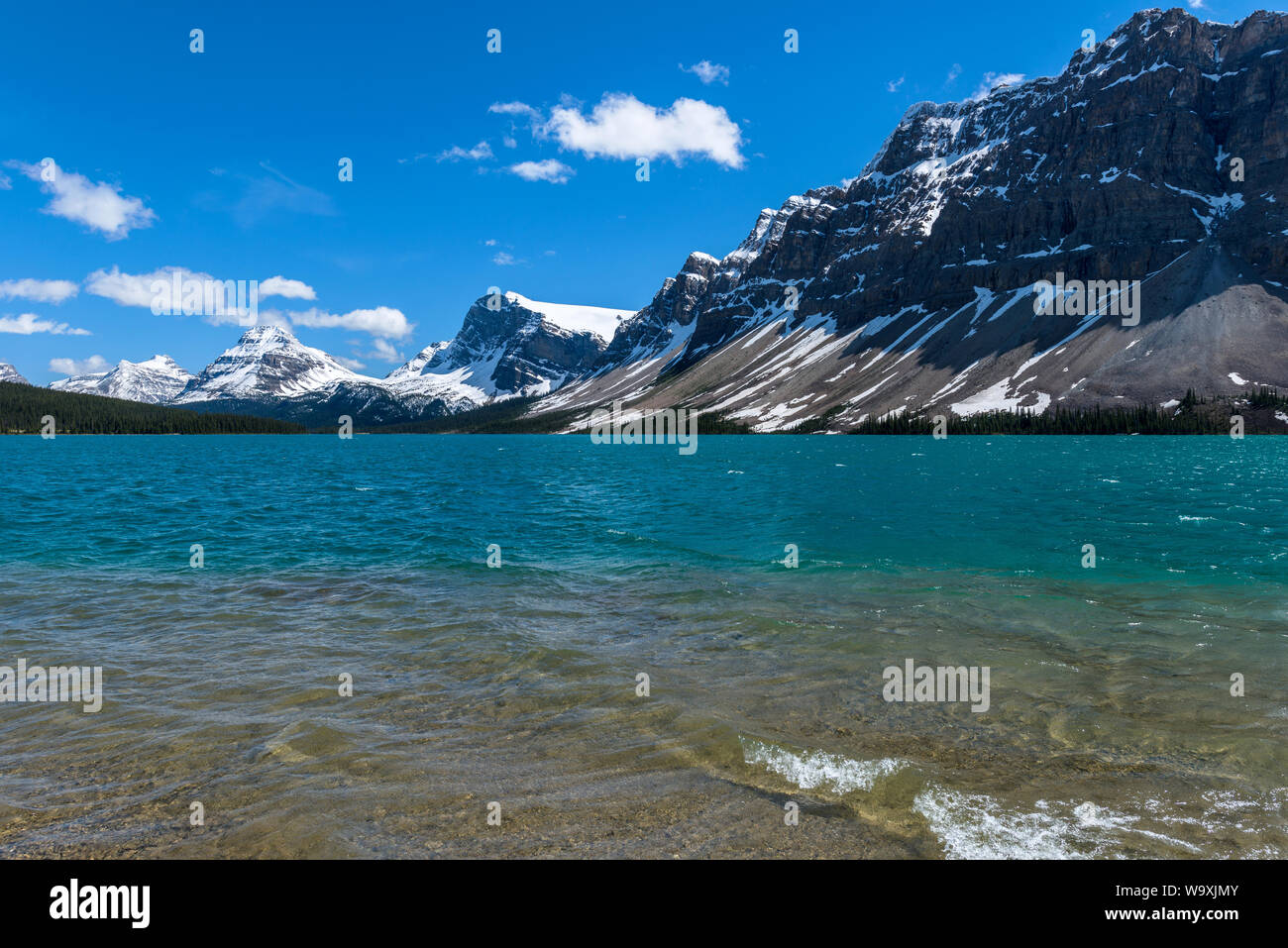 Bow Lake - A sunny Spring day view of crystal-clear and colorful Bow Lake, surrounded by snow-capped high peaks, at Banff National Park, AB, Canada. Stock Photo