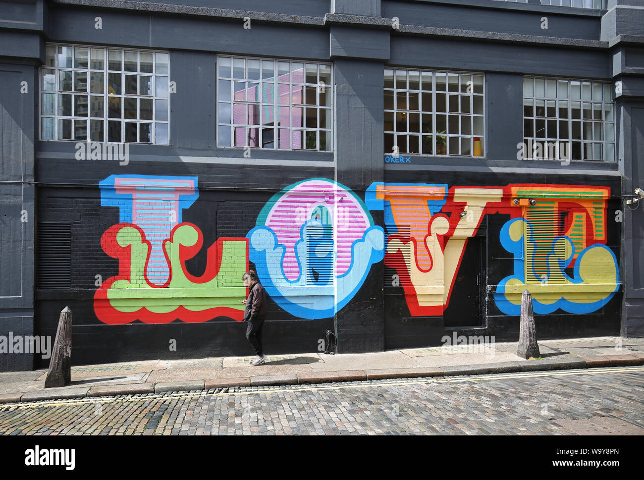 A man walks past the word LOVE painted onto an industrial building in Ebor Street in Shoreditch, London, UK. Brightly coloured,1960's syle lettering. Stock Photo
