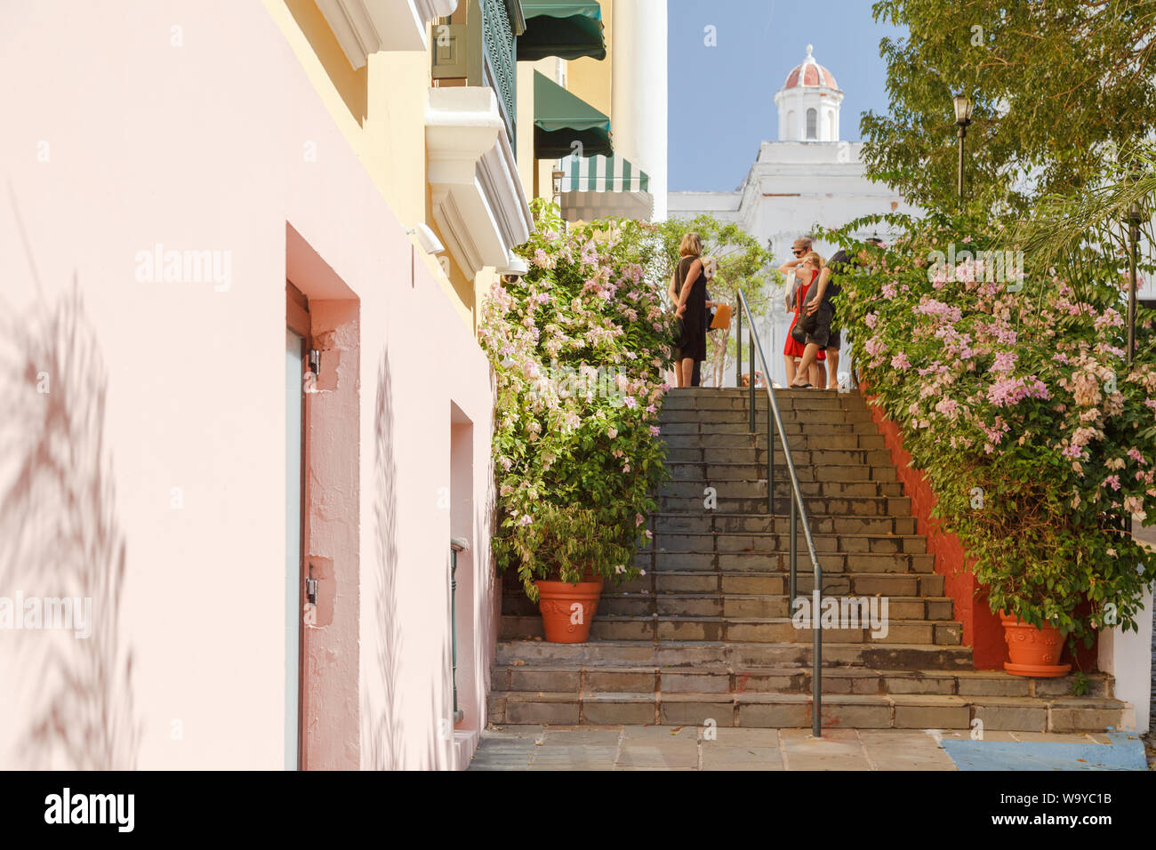 People chat on top of the flower filled stairs at Plaza de la Catedral located in front of San Juan Bautista Cathedral in Old San Juan, San Juan, PR. Stock Photo