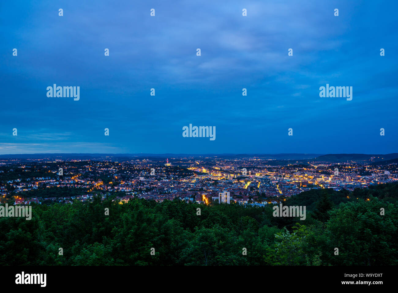 Germany, Magic lights of houses of big city stuttgart from above behind green forest in beautiful twilight mood from mount rubble Stock Photo