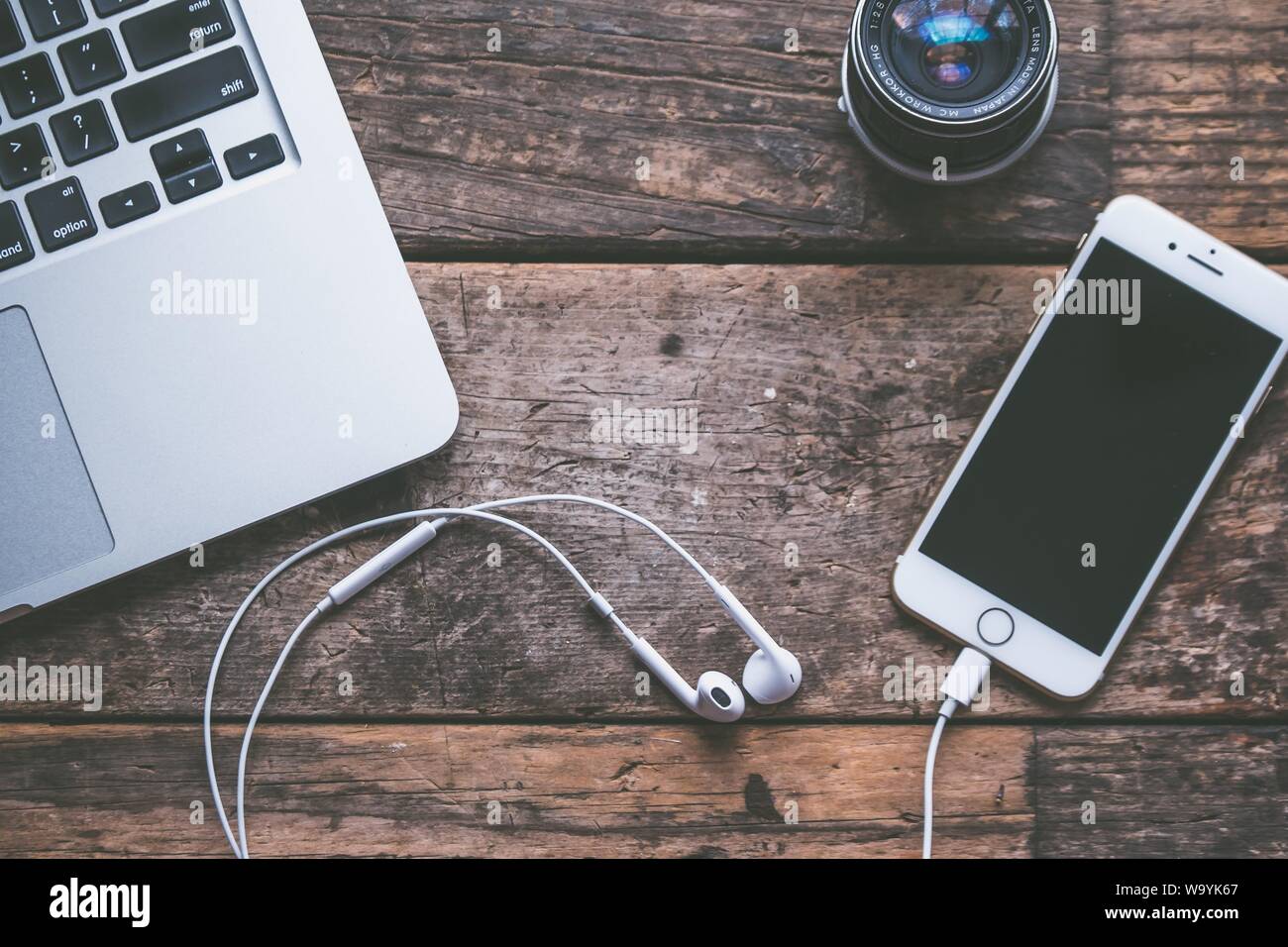 Closeup shot of a laptop with a smartphone and headphones on a wooden background and a camera lens Stock Photo