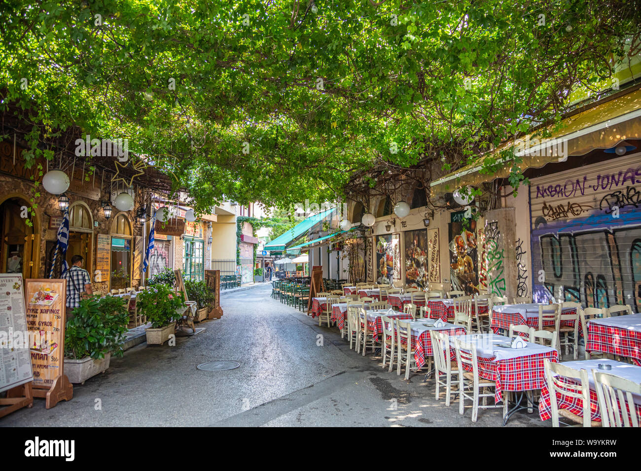 Athens, Greece - August 4, 2019: Plaka, narrow street with lush greenery and outside greek tavern tables in historical center Stock Photo