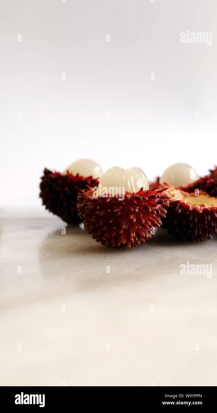 Peeled pulasan fruits in vertical photo. Scientific name Nephelium ramboutan-akea, pulasan is a red tropical fruit that is closely allied to rambutan. Stock Photo