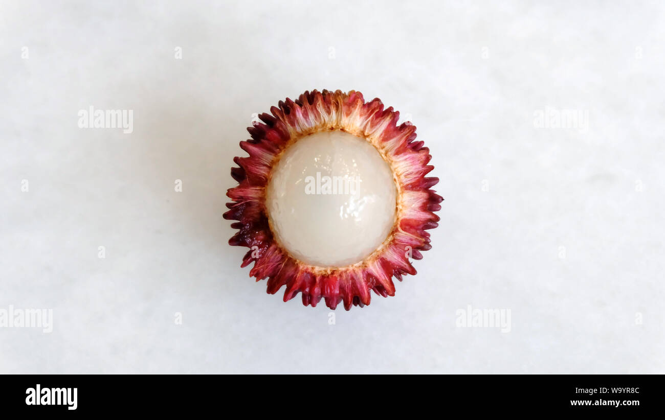 A single pulasan fruit with the skin peeled off and inner white flesh visible. It is a red tropical fruit that is closely allied to rambutan. Stock Photo
