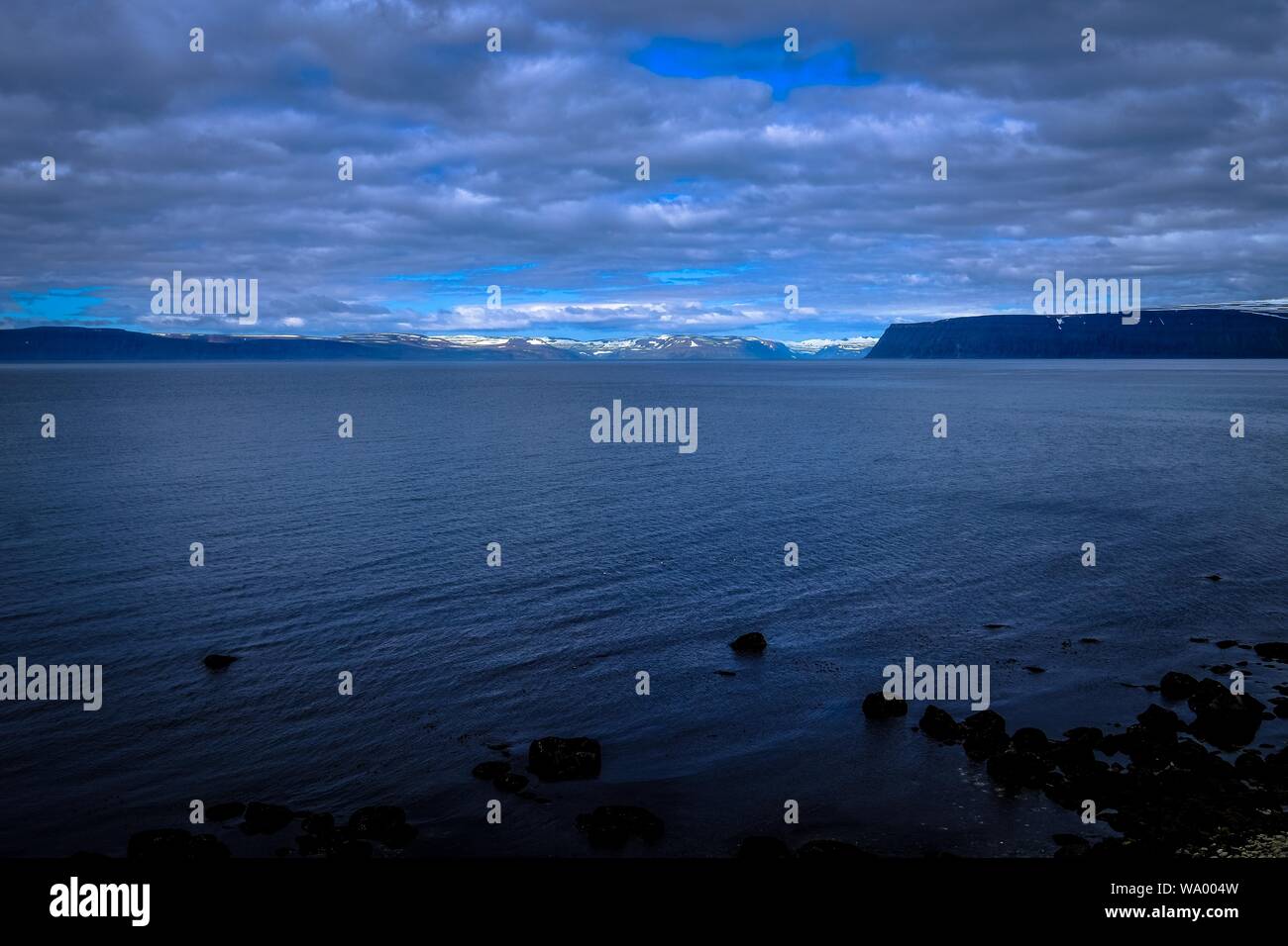 Beautiful shot of a sea and mountains in the distance under a cloudy sky Stock Photo