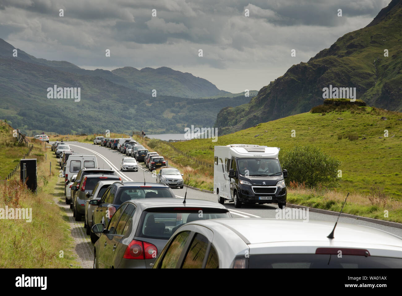 Congestion in Snowdonia, North Wales, 15th August 2019. Cars parked legally on the A498 - the Nant Gwynant pass, convenient for walkers to access the Pyg Track and Miners Track, leading to the peak of Snowdon. The popularity of the national park in summer means that many tourists drive to the area, there is a lot of traffic and these car parks are often full. The pass descends to Llyn Gwynant and to another car park popular with people that climb Snowdon via the Watkins Path. This road also leads to the beautiful village of Beddgelert and the picturesque Llyn Dinas. Stock Photo