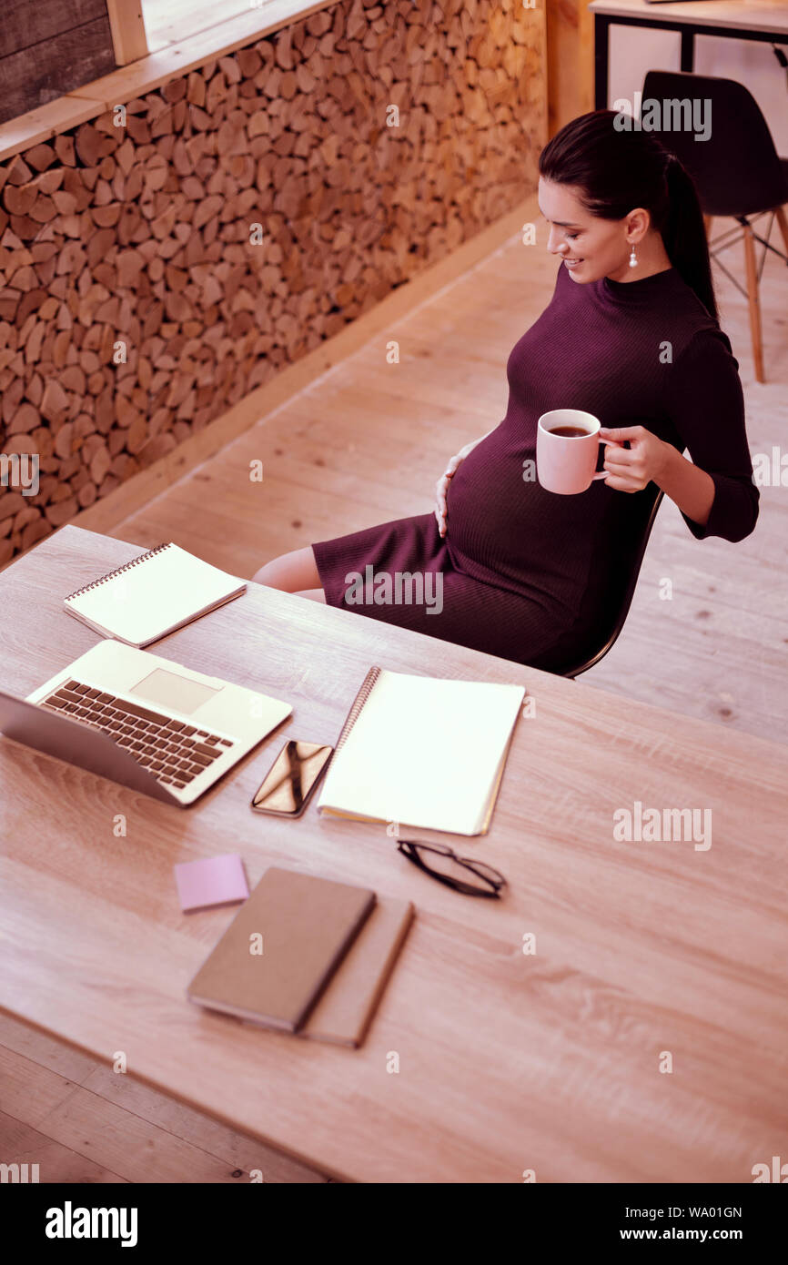 Dreamy mood. Kind woman keeping smile on her face while feeling movements in belly Stock Photo