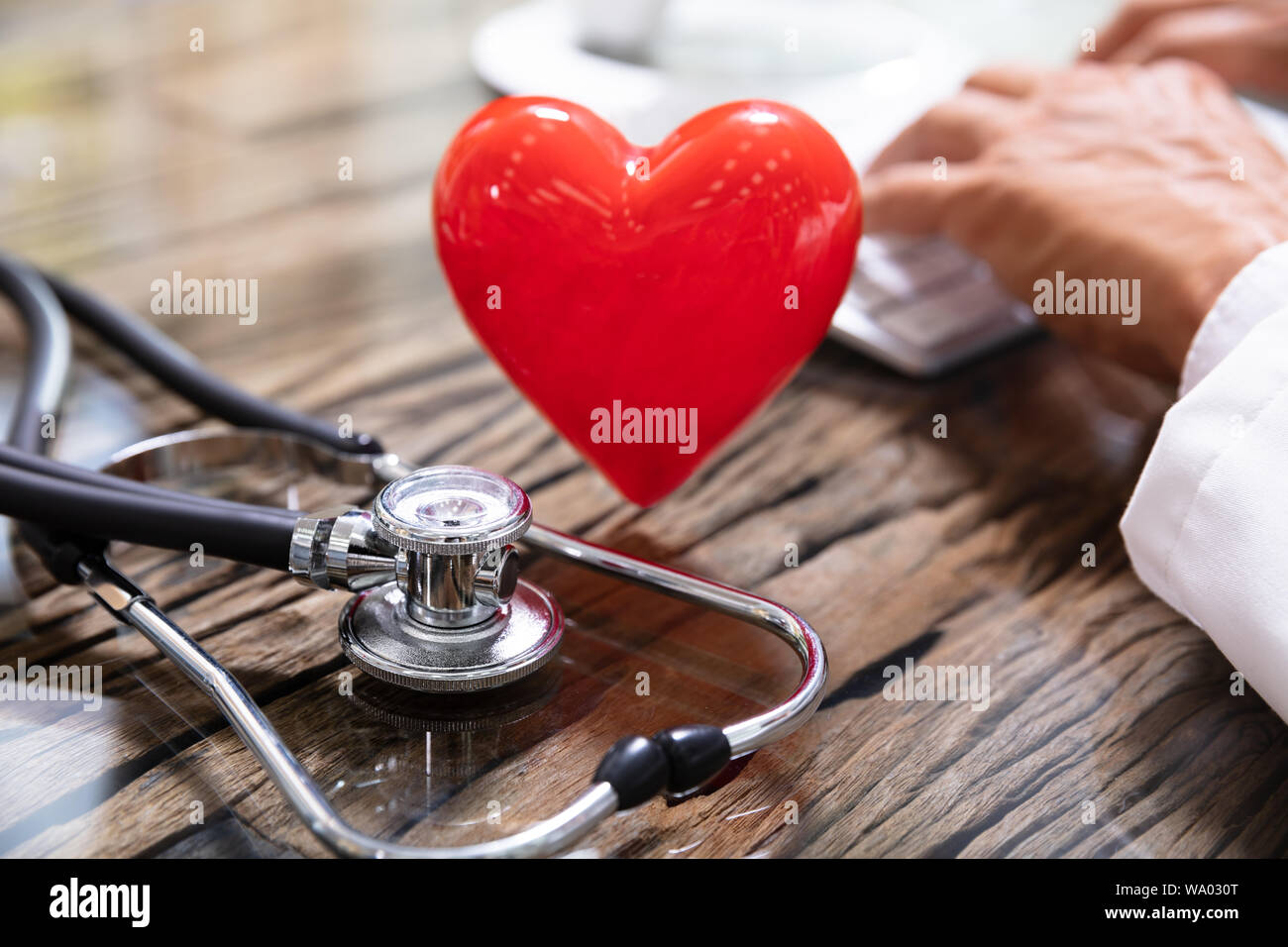Red Heart With In Front Of Doctor Working On Computer Stock Photo - Alamy