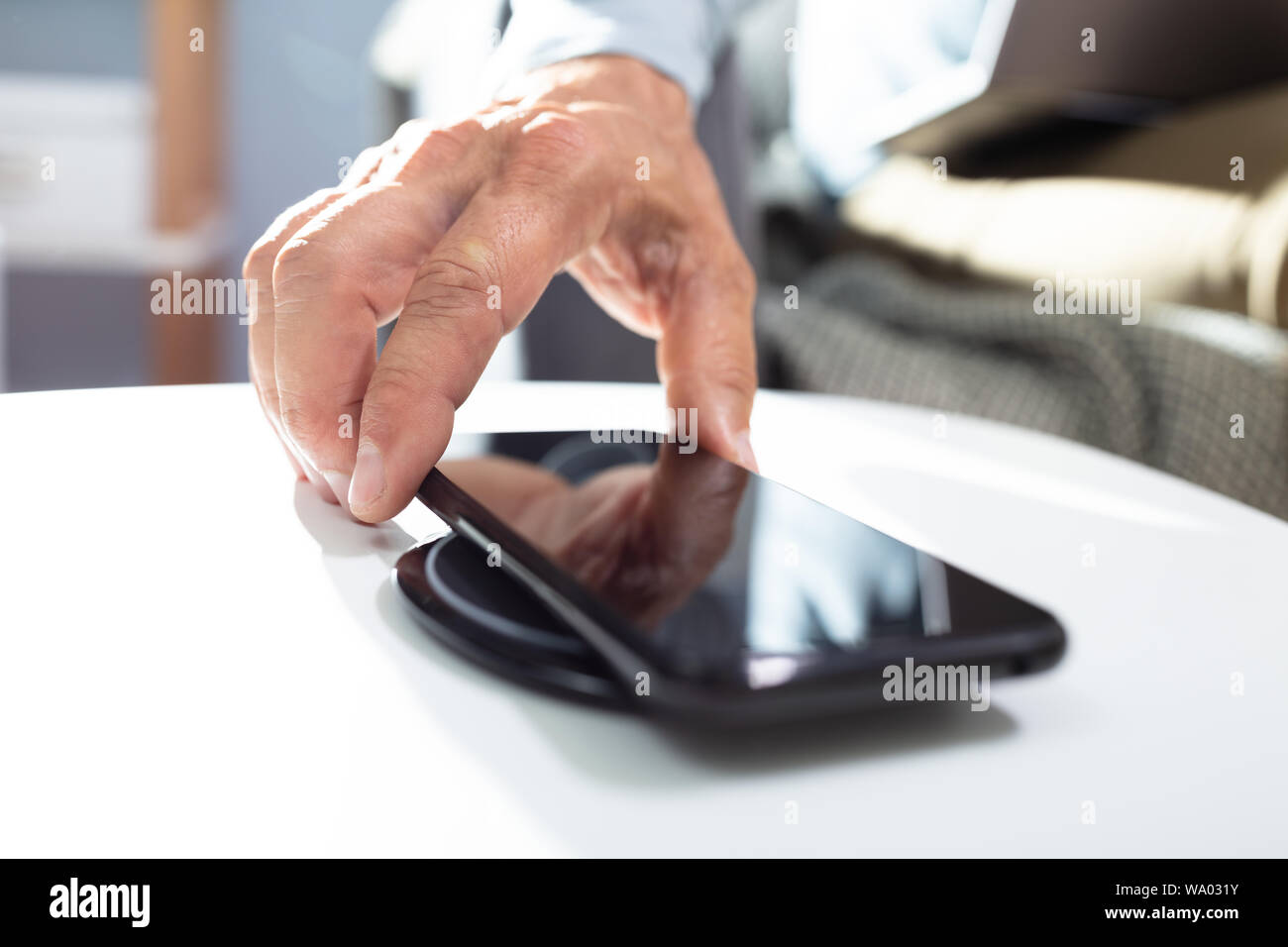 Man Charging Smartphone Using Wireless Charging Pad At Home Stock Photo