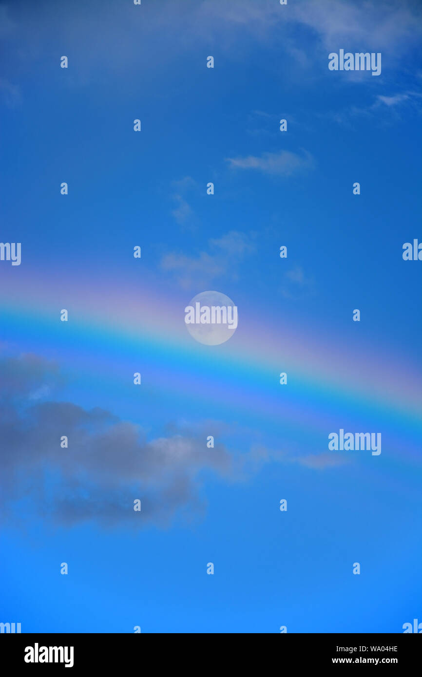 Skyscape with full moon and rainbow against the blue sky Stock Photo