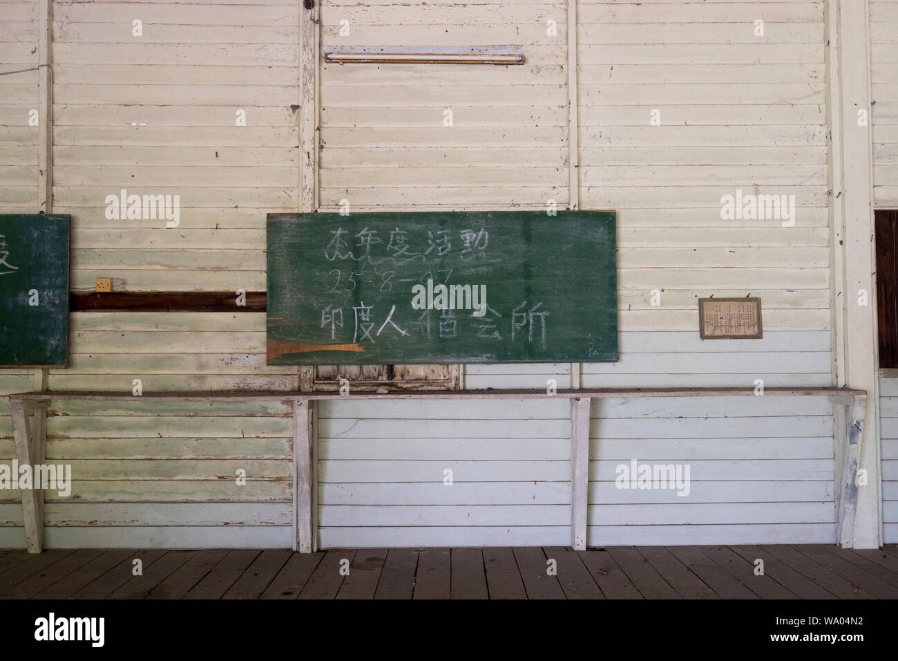 A green chalkboard with Chinese lettering is mounted on the wall of an old, wooden, colony-era hall in Port Dickson, Malaysia. Stock Photo