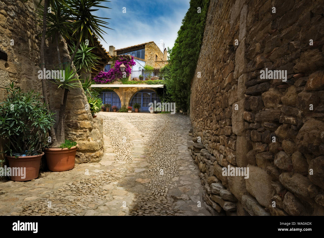 The bright purple Bougainvillea on the walls of a typical Peratallada house contrasting with the blue paintwork and soft red stone work Stock Photo