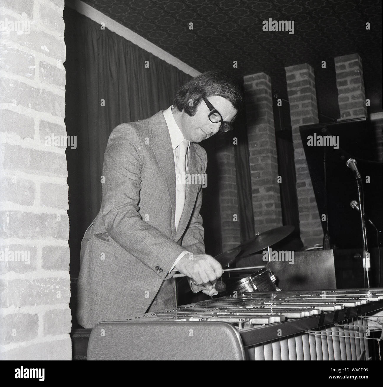 1960s, historical, a musician in a suit and tie witht yarn coated wooden mallets in his hands playing the marimba in an indoor venue, London, England, UK. The marimba, a percussion instrument similar to the xylophone, has a set of wooden bars that when struck produce musical tones. The pipes suspended underneath the bars ampify the sound. Stock Photo