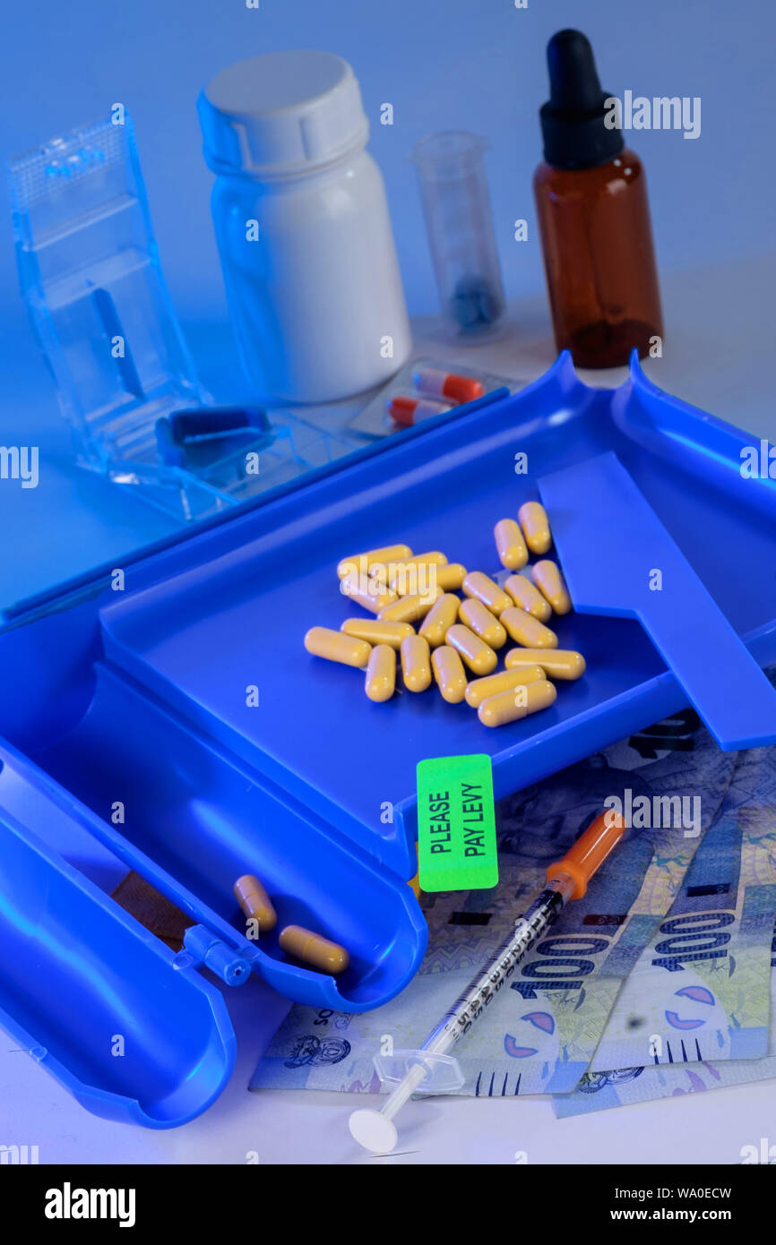 Pharmaceutical counter with tables and please pay levy sticker on, money in the foreground and pill boxes in the background Stock Photo