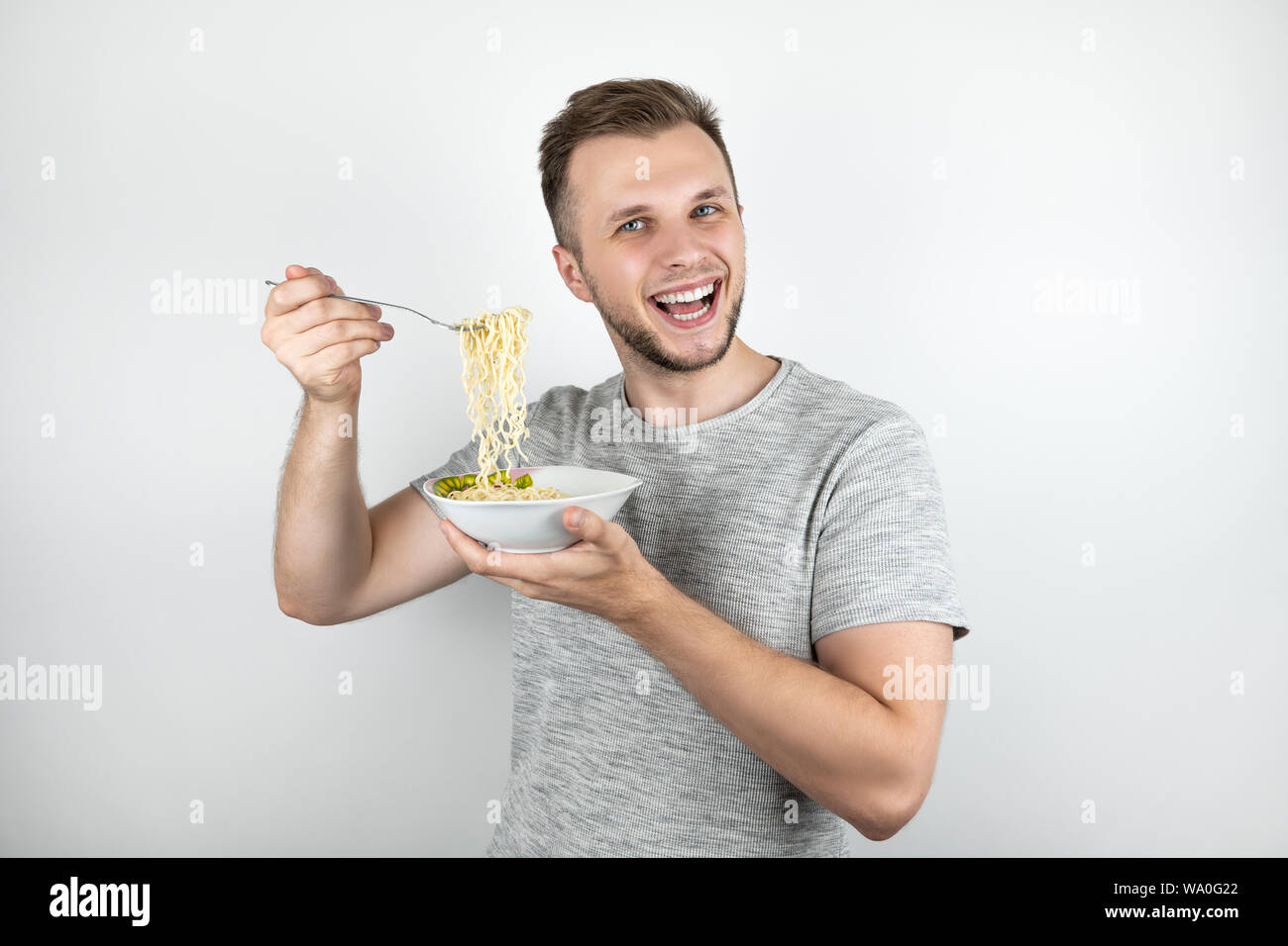 young handsome man eating noodles with fork looking hungry on isolated