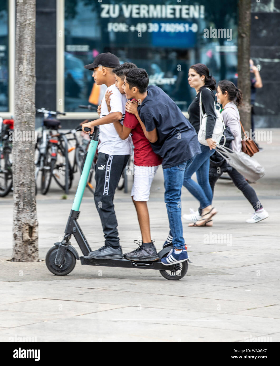 electric rental scooter, driving, at Alexander Platz, Berlin, 3 people on one scooter Stock Photo Alamy