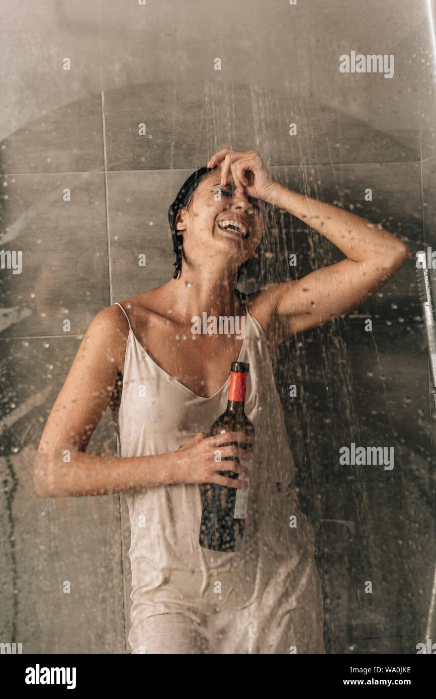 lonely depressed woman in shower holding wine bottle and crying at home