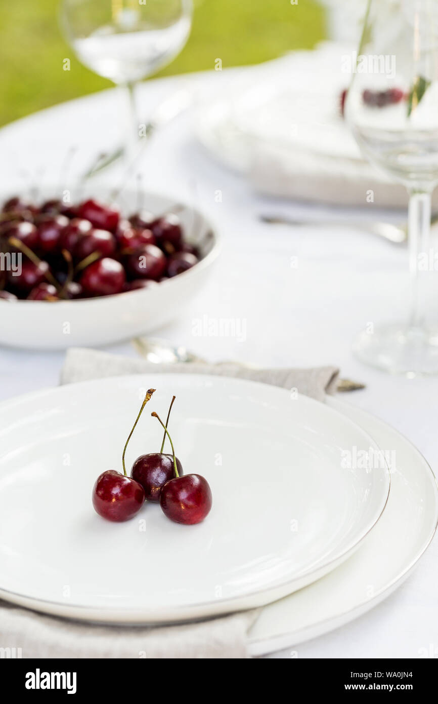 Serving plate with sweet cherry as decor with white tablecloth and tableware. Concept of holiday table set Stock Photo