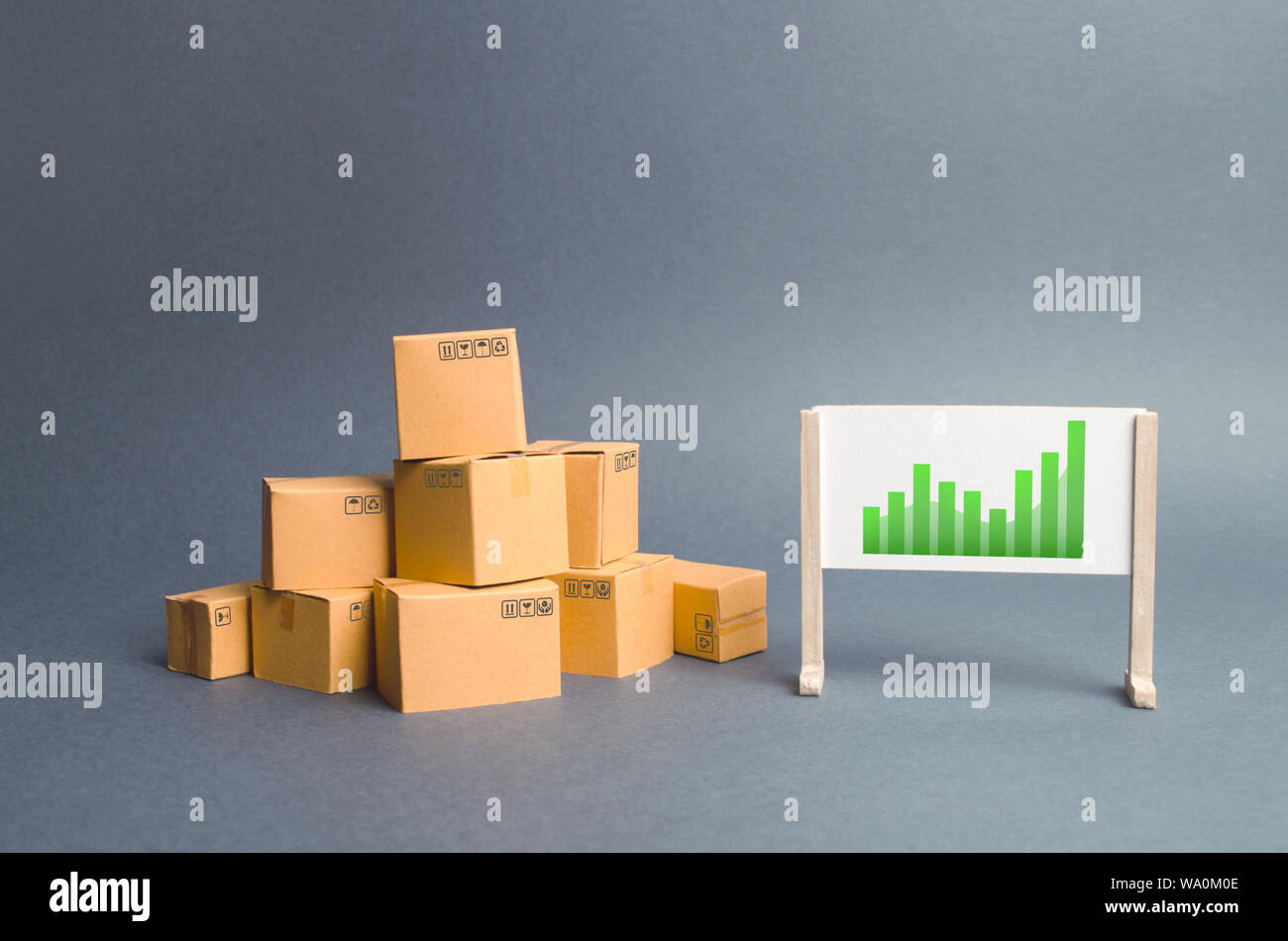 Plenty of cardboard boxes and whiteboard with green positive trend chart. rate growth of production of goods and products, increasing economic indicat Stock Photo