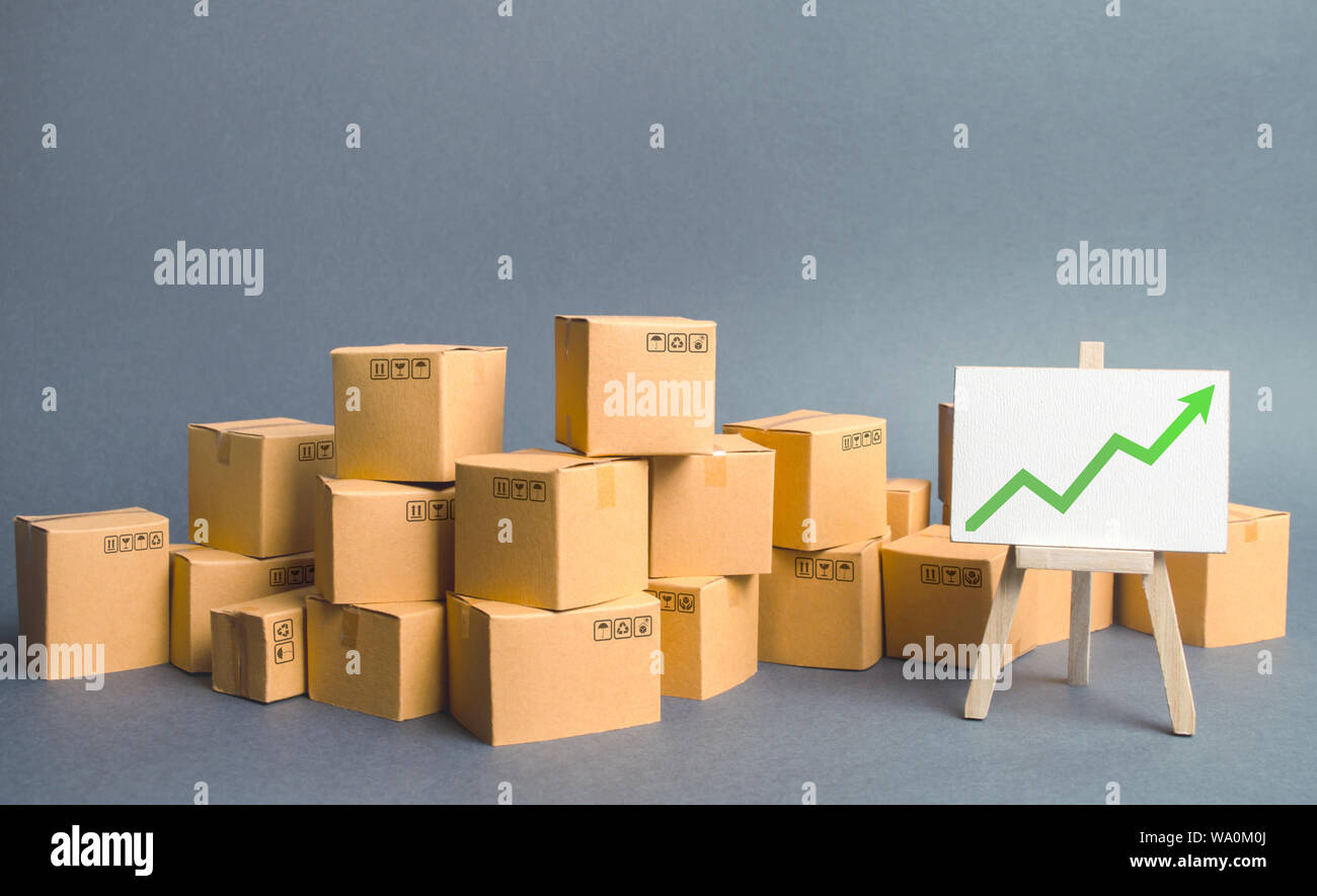 A large number of cardboard boxes and sign with green up arrow. rate growth of production of goods and products, increasing economic indicators. Incre Stock Photo