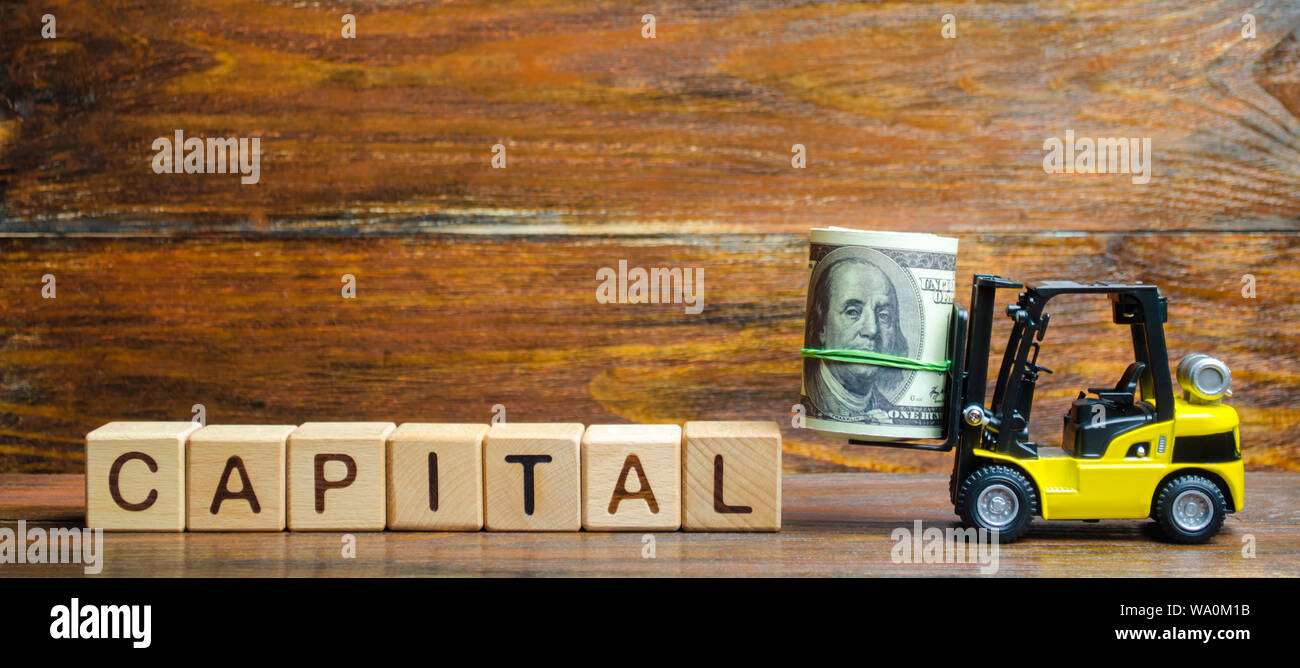 Yellow forklift truck carries a bundle of dollars to inscription CAPITAL. Increasing the attractiveness of the conditions for business, increasing the Stock Photo