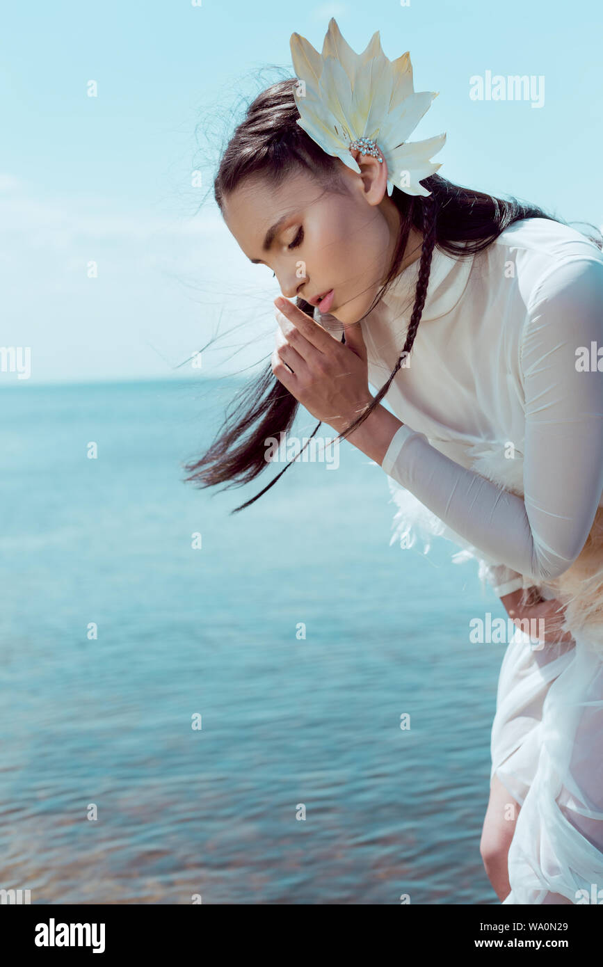 brunette woman in white swan costume holding finger near lips, making shh sign Stock Photo