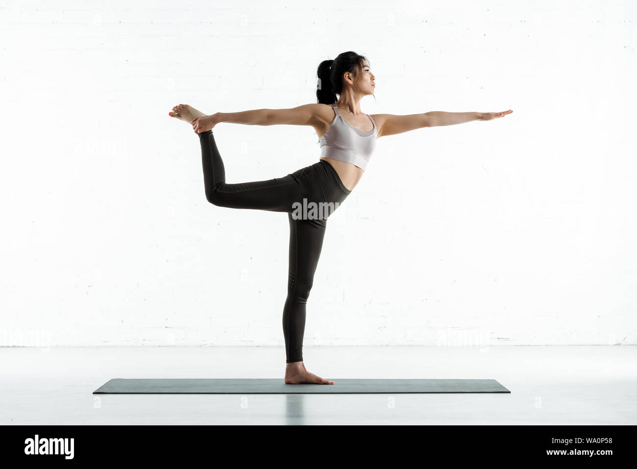 Calm Thai Woman Standing On Yoga Mat And Doing Exercise On White