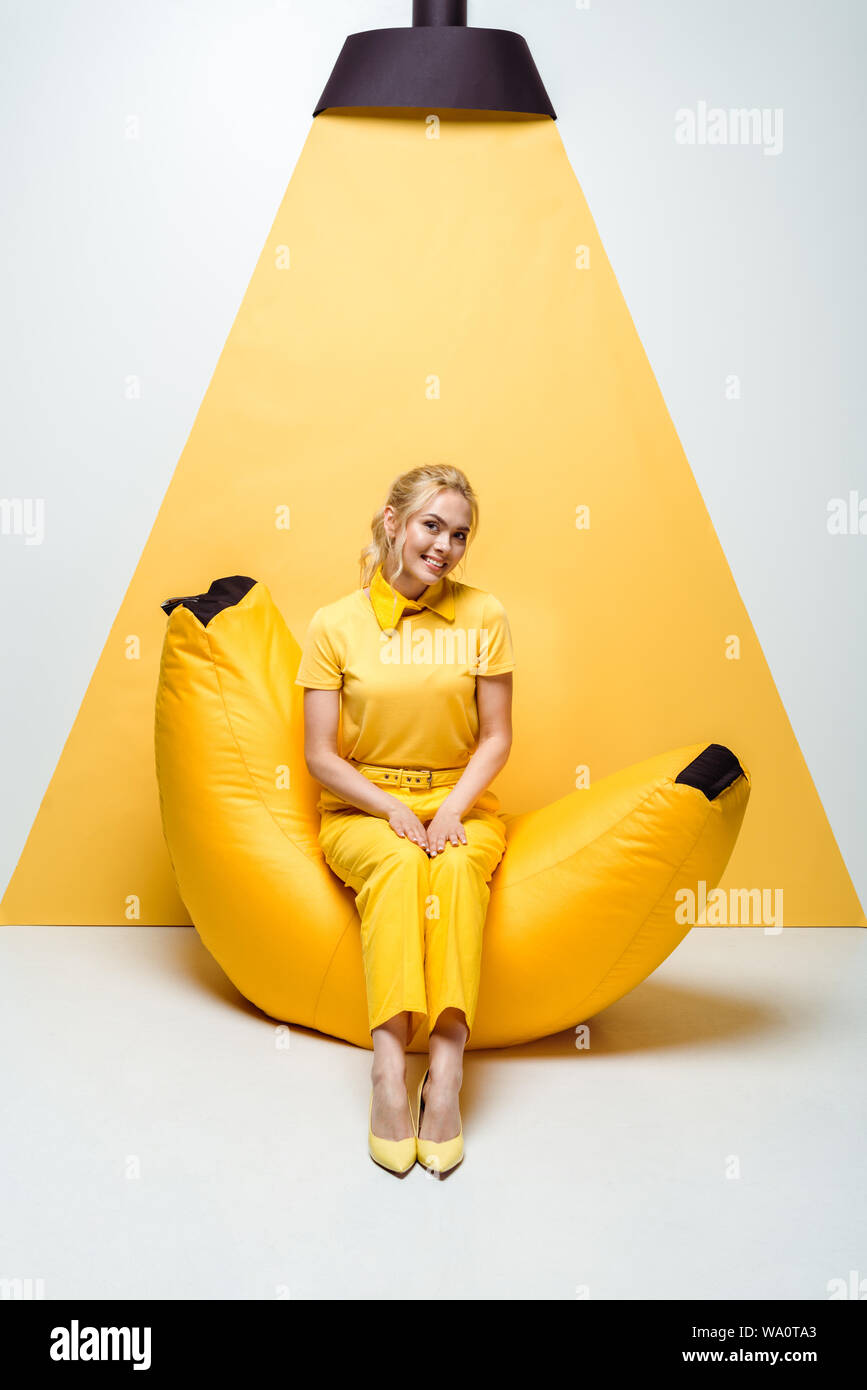 happy blonde woman sitting on bean bag chair on white and yellow Stock ...