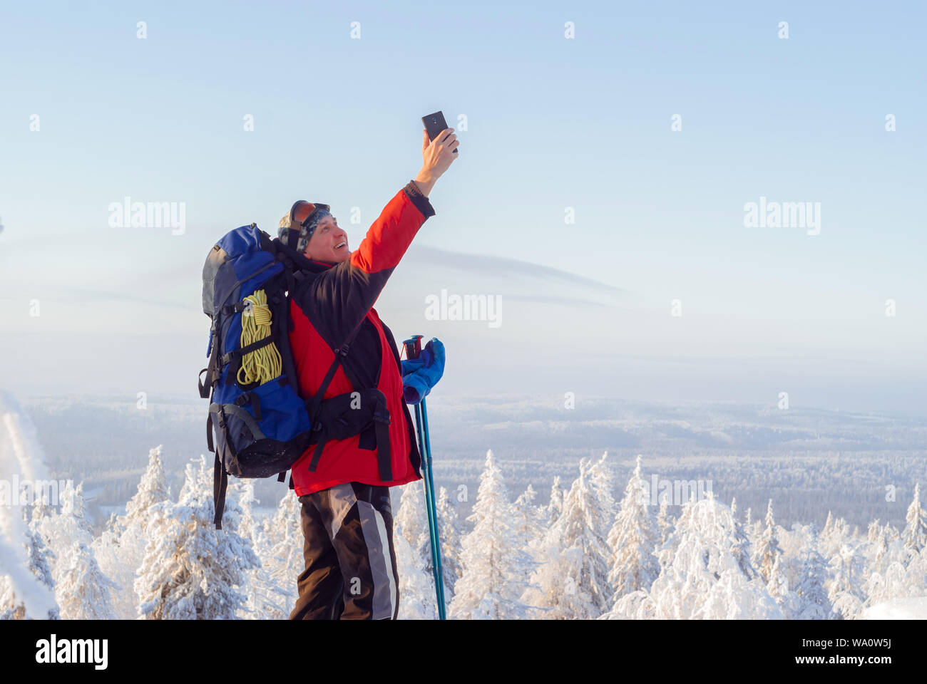 hiker on top of a mountain in winter catches a signal by raising his hand with a smartphone up, or simply takes a selfie Stock Photo