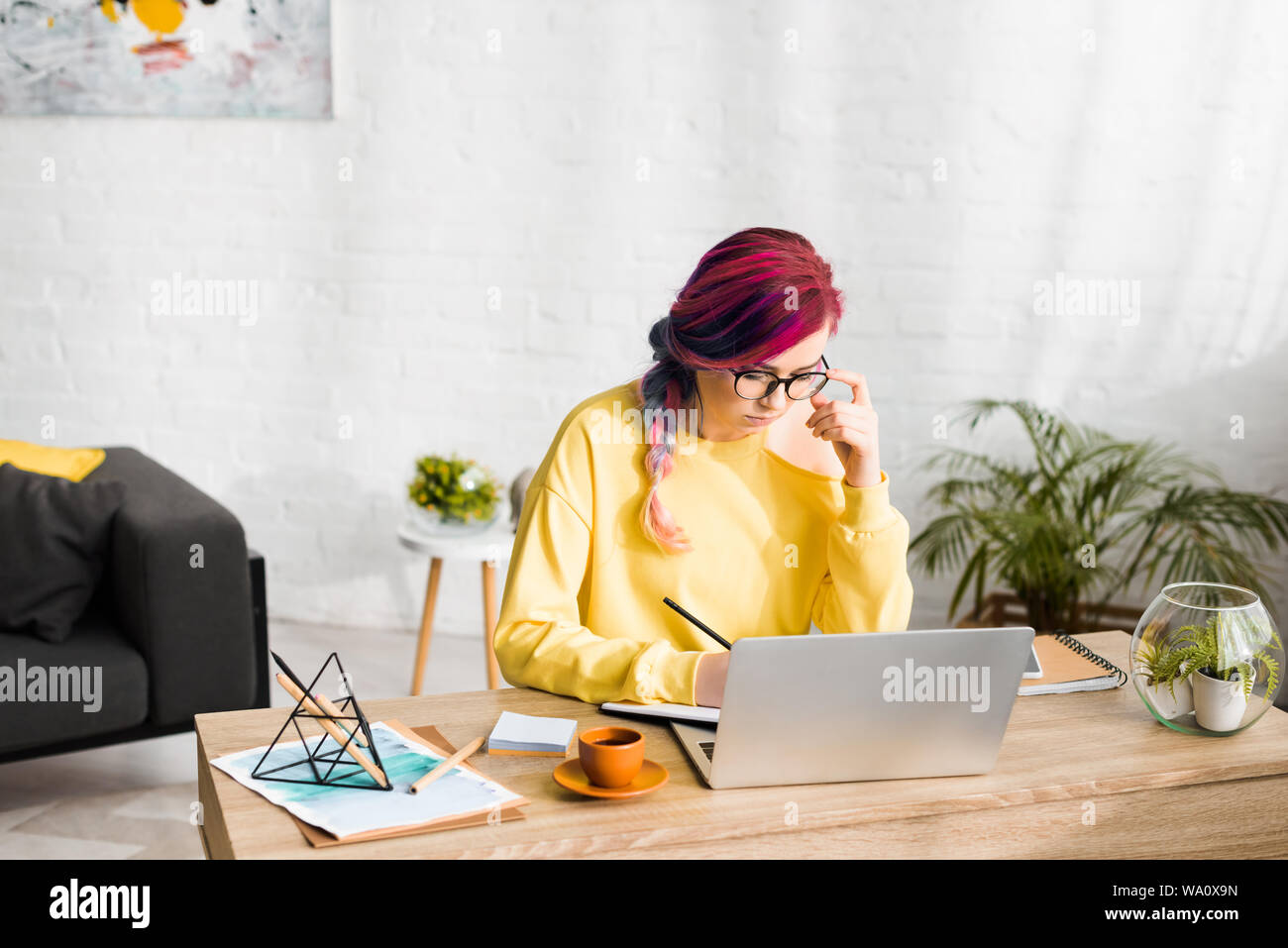 hipster girl pensively making notes while sitting behind table in living room Stock Photo