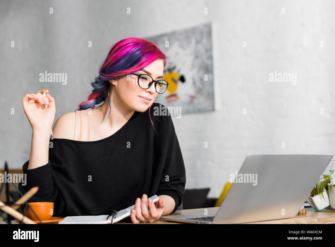 girl with colorful hair sitting at desk and making notes in living room Stock Photo