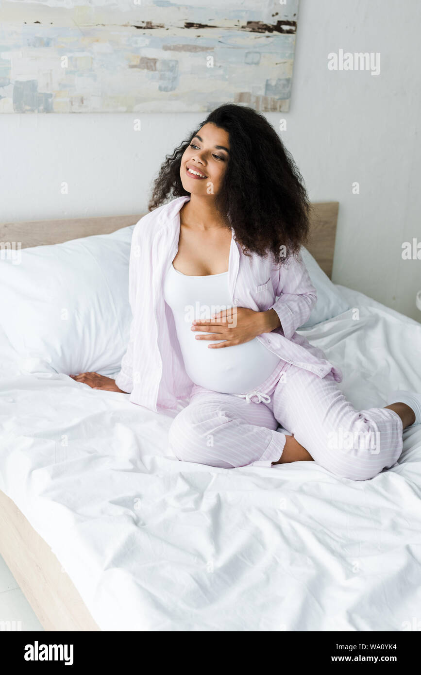 Positive Young Pregnant African American Woman Sitting On Bed And ...