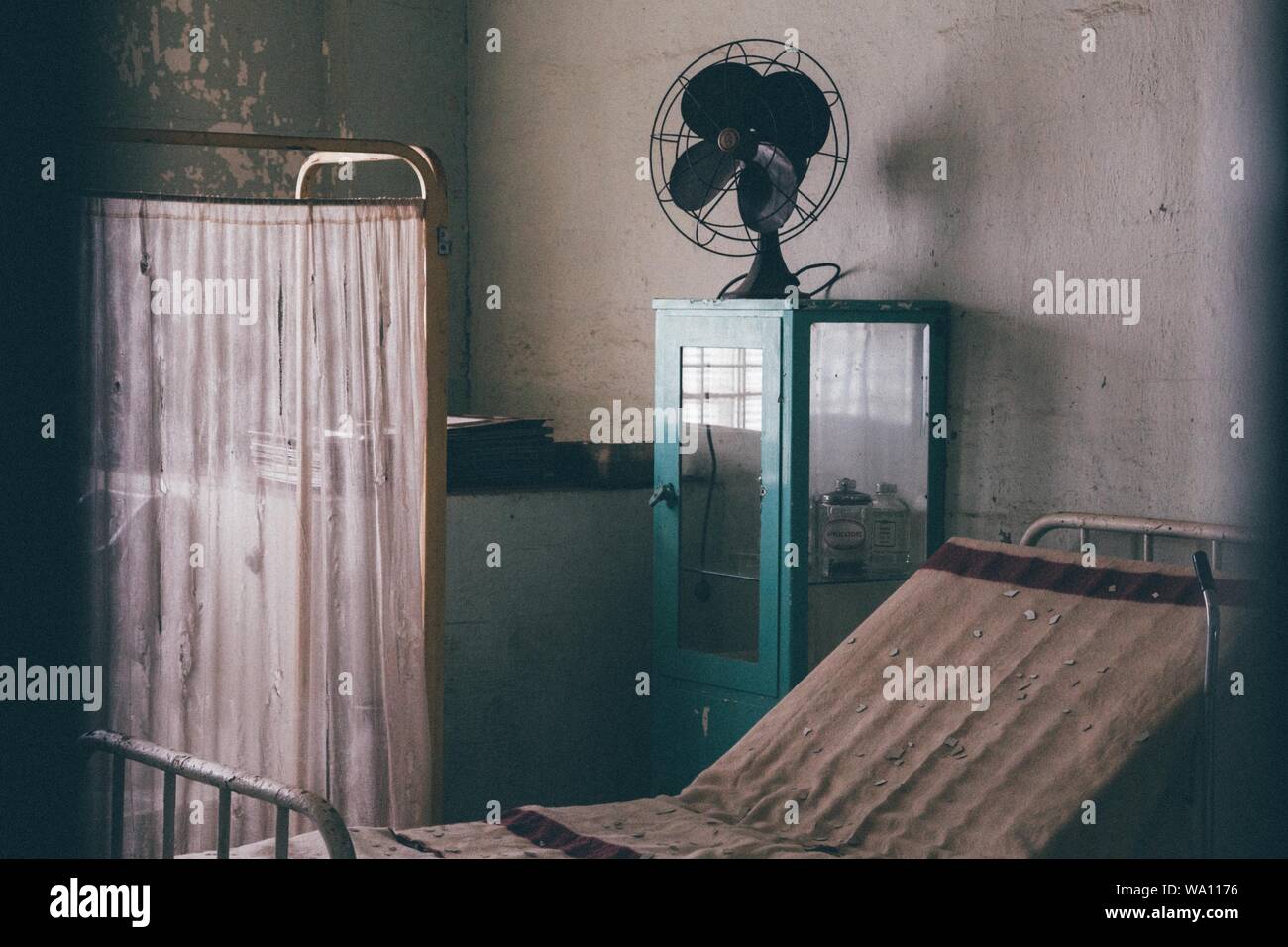An Old Hospital Bed And Curtain Near A Blue Medicine Cabinet With