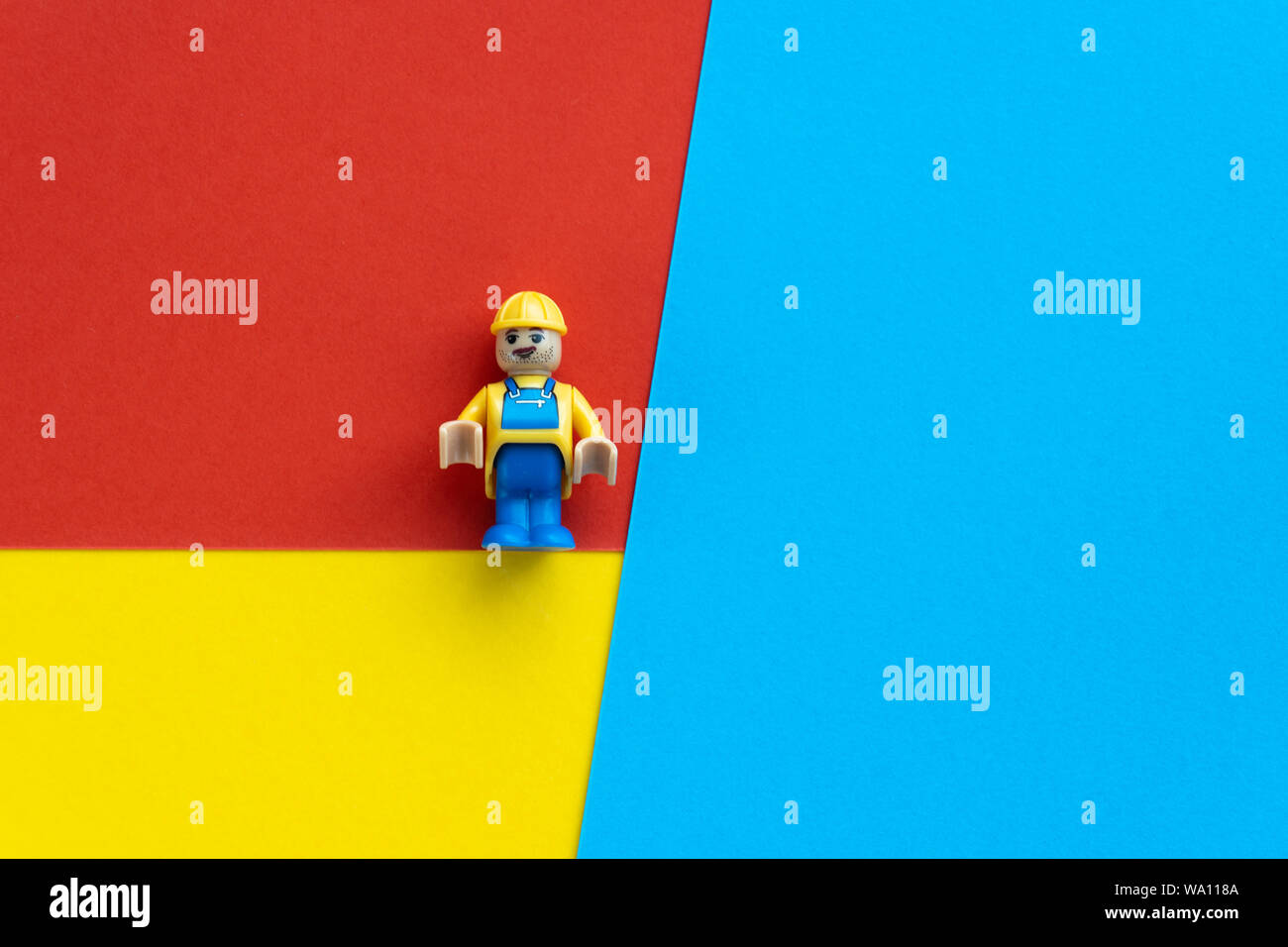 Milan, Italy - August 11 2019: Lego toy of engineer construction worker with helmet on multicoloured paper background, geometric flat composition. Fix Stock Photo