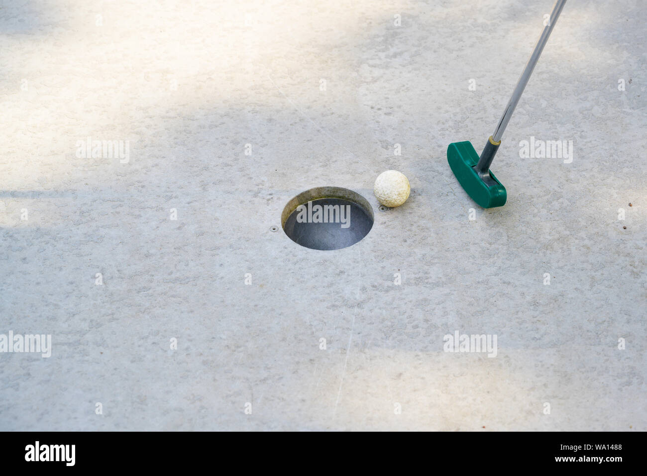 mini golf club hits the ball into the hole on a track from concrete, copy space, selected focus Stock Photo