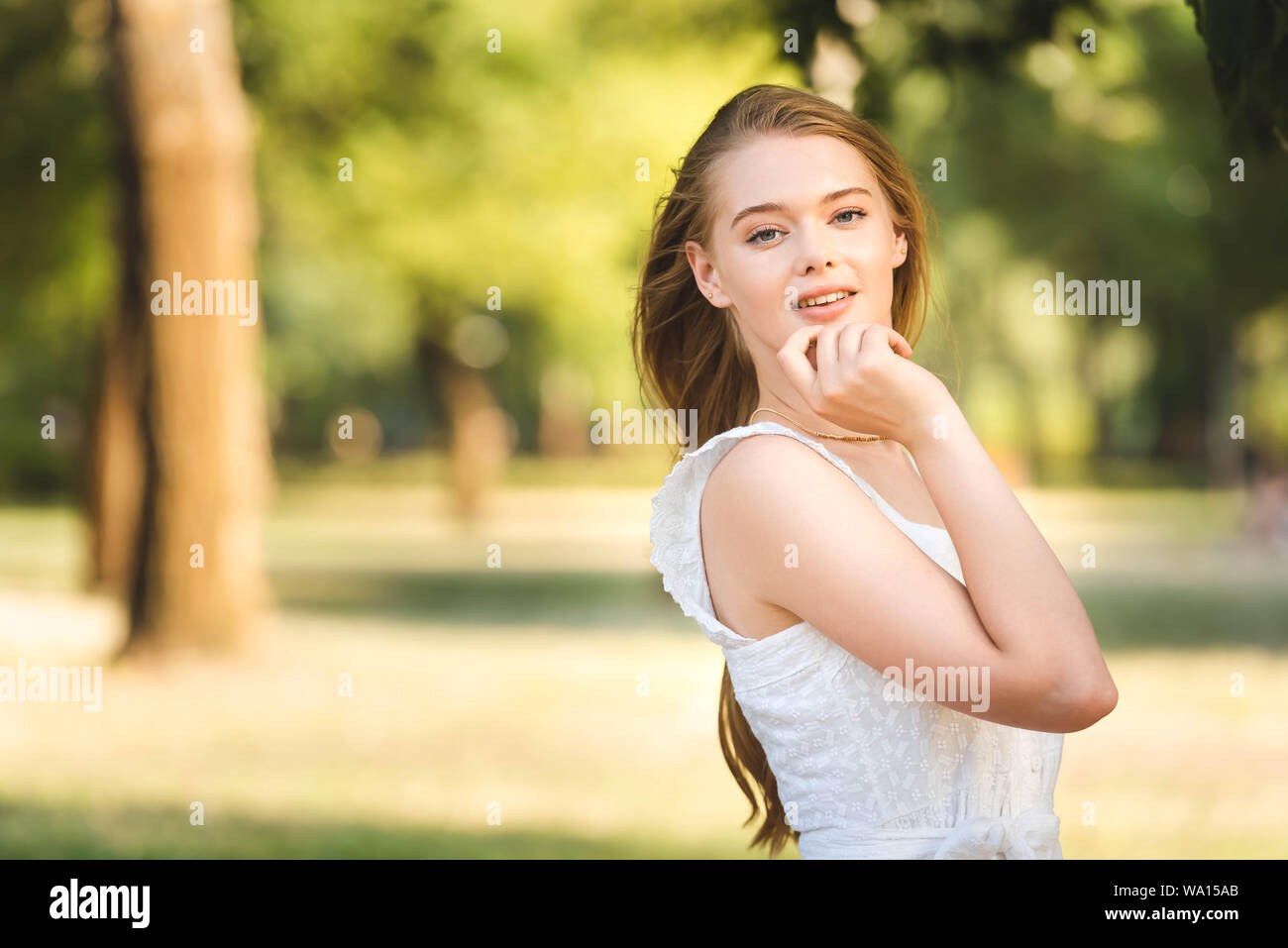 front view of beautiful young girl in white dress posing while standing ...