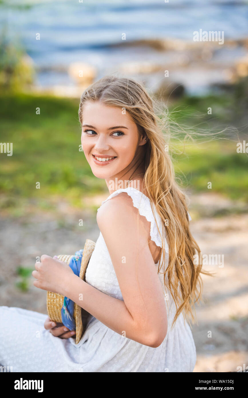 portrait shot of beautiful girl in white dress holding straw hat ...