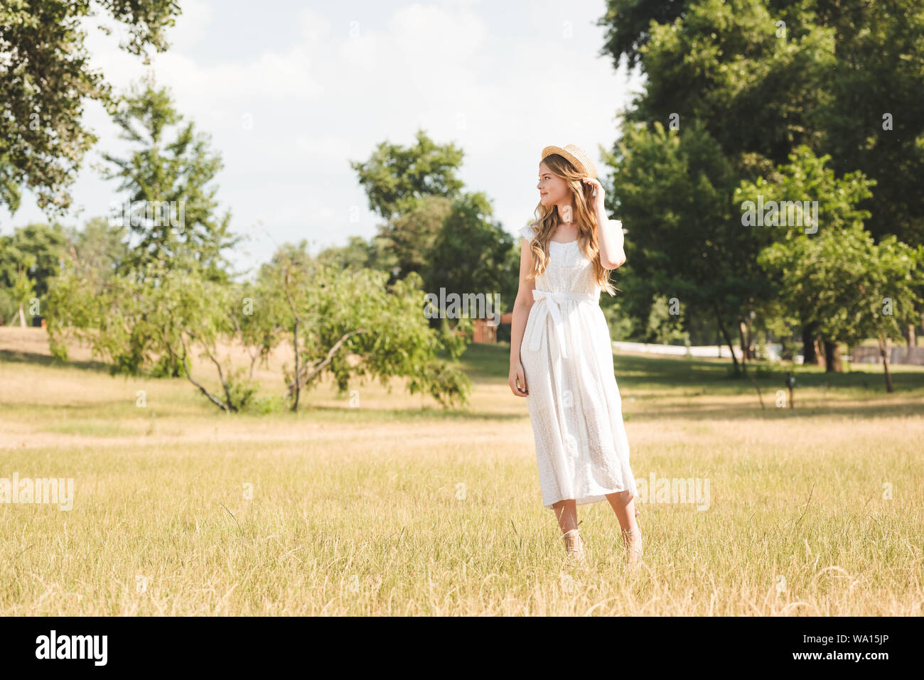beautiful girl in white dress and straw hat standing on meadow and ...