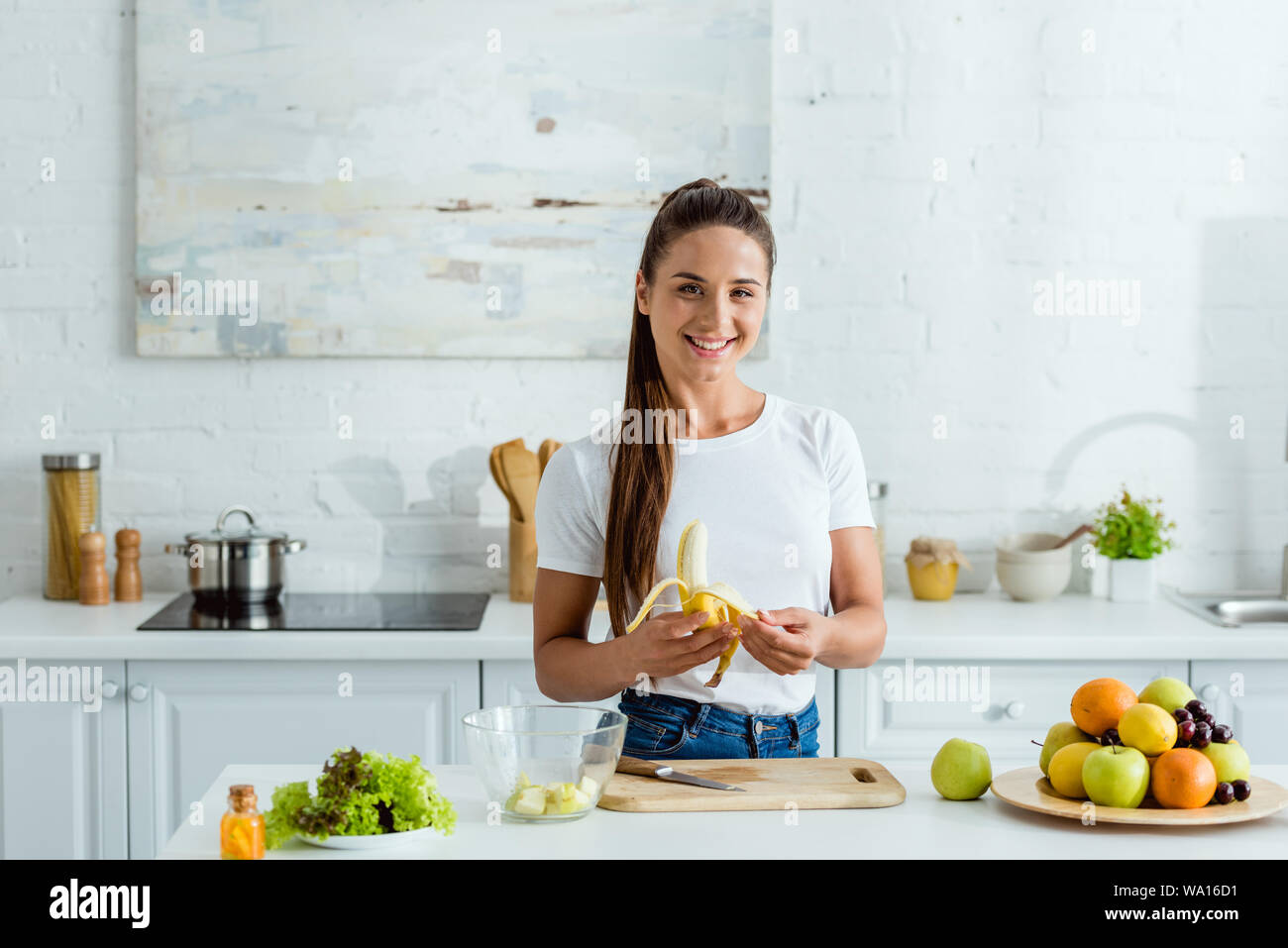 happy girl cutting banana on peeling board near tasty fruits Stock Photo