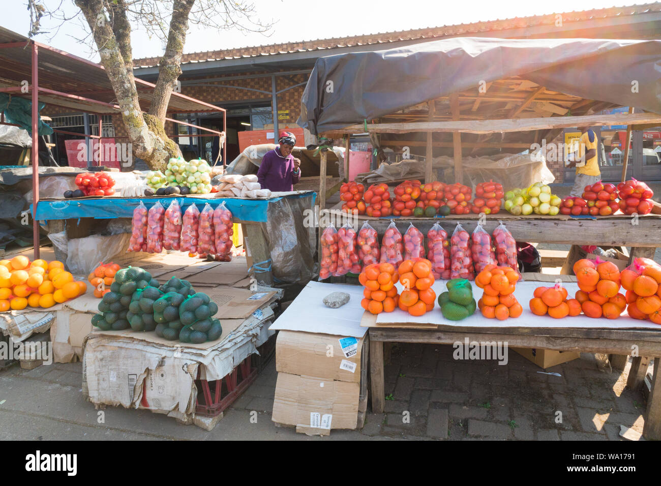 Black African lady or woman at her street vendor stall which displays a selection of bags of fruits and vegetables in Graskop,Mpumalanga, South Africa Stock Photo